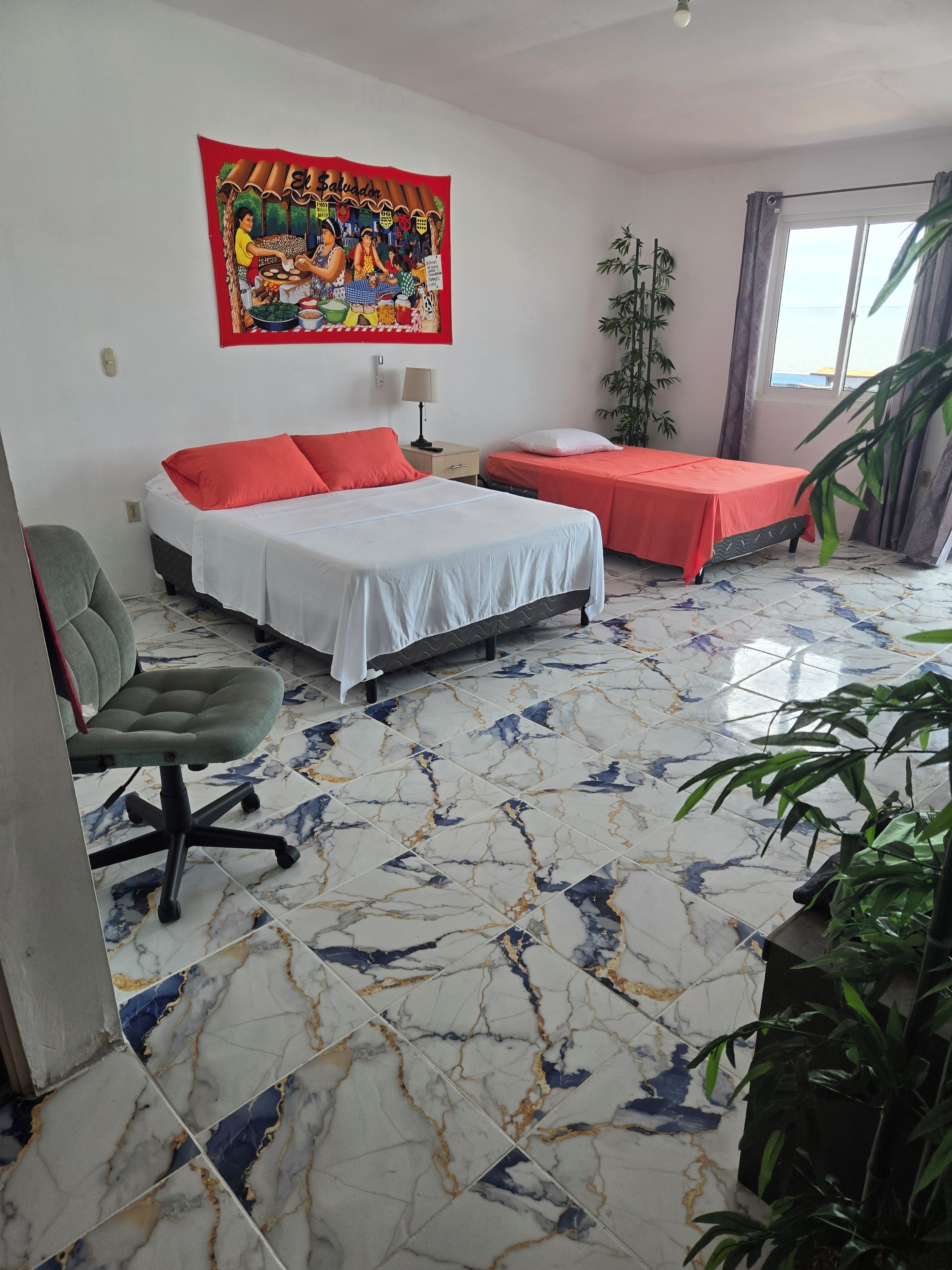 A hotel room with a bed, a desk, a chair, a window, and a painting on the wall.