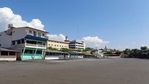 Un hotel frente a la playa con varias edificaciones, incluyendo un edificio blanco destacado con techo azul y una estructura más pequeña con techo verde.