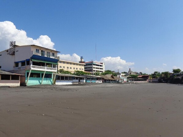 Um hotel à beira-mar com vários edifícios, incluindo um prédio branco imponente com telhado azul e uma estrutura menor com telhado verde.