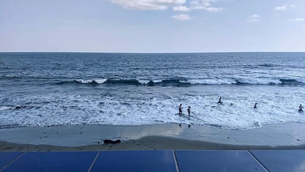 Una playa con olas y gente nadando.