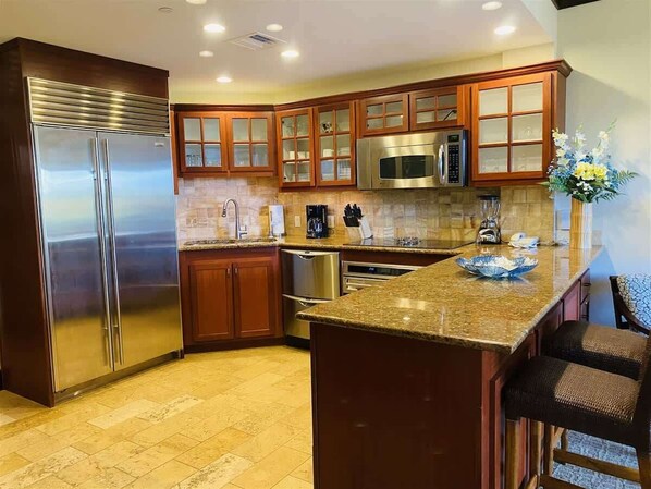 A modern kitchen with stainless steel appliances, wooden cabinetry, and a granite countertop.