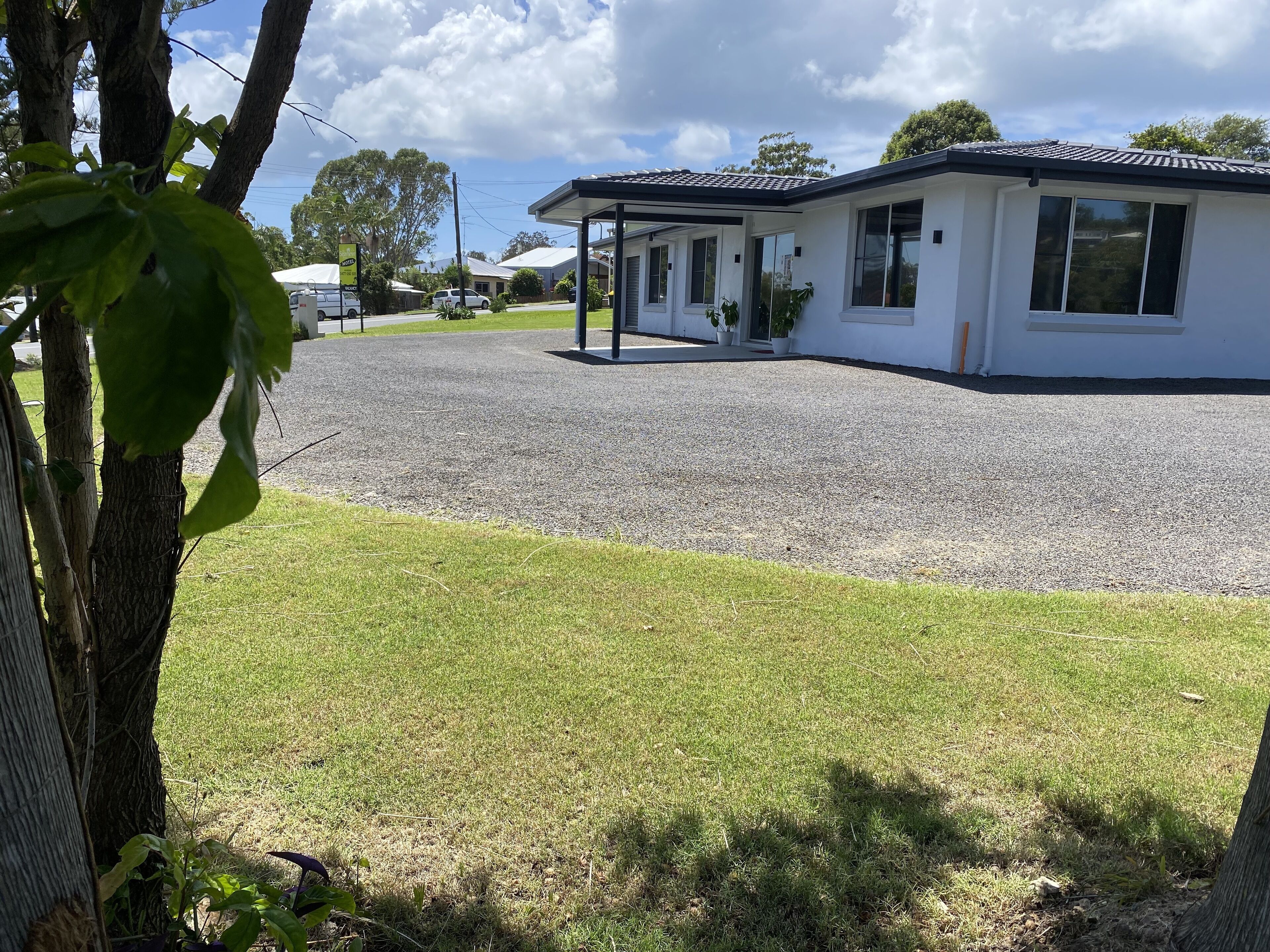 A modern building with a covered outdoor area, a gravel driveway, and a grassy lawn.