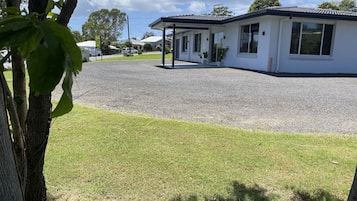 A modern building with a covered outdoor area, a gravel driveway, and a grassy lawn.