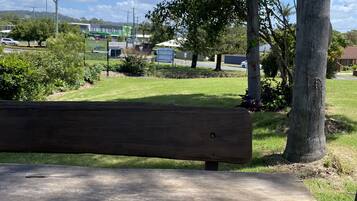 A wooden bench in a park with trees and a grassy area.