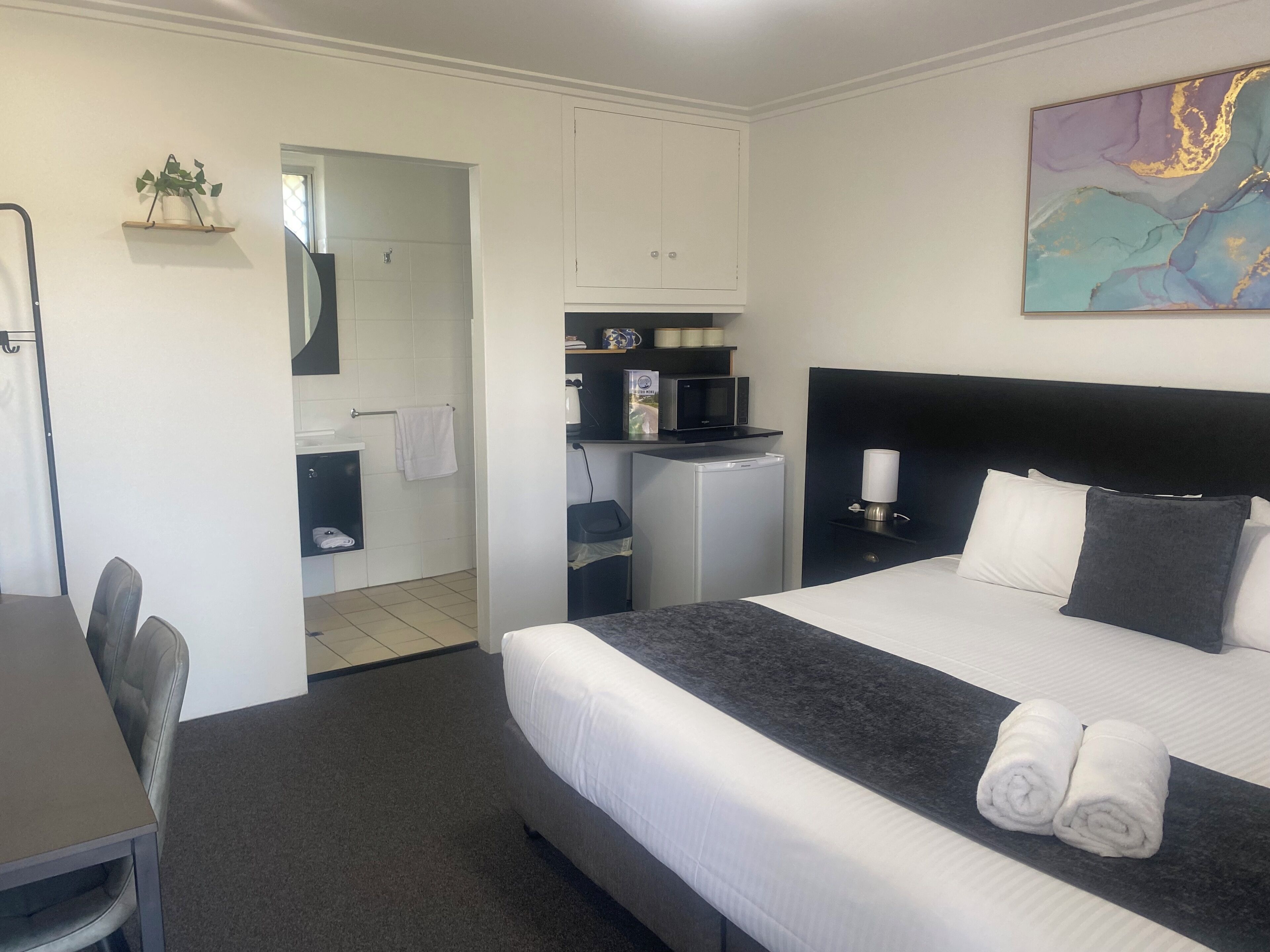 A hotel room with a bed, a desk, a chair, a small kitchenette, and a bathroom.