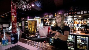 Un barman sert des boissons dans un bar, avec des étagères remplies de bouteilles en arrière-plan.