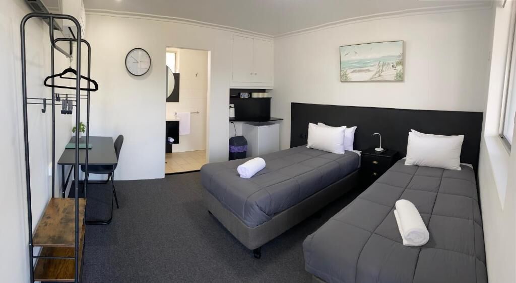 A hotel room with two beds, a desk, a chair, a TV, and a painting on the wall.