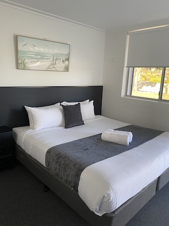 A neatly made bed with white and gray linens, a dark headboard, and a painting of a beach scene on the wall.