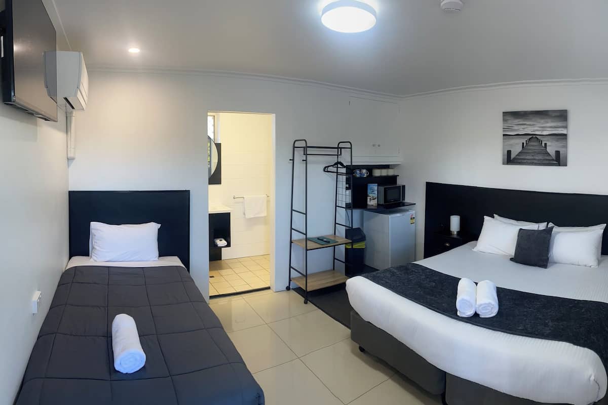 A hotel room with two beds, a TV, a small kitchenette, and a view of the outside.