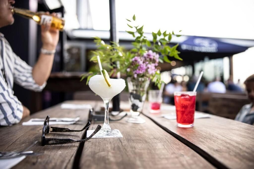 A wooden table with a martini glass, a red drink, and a pair of glasses.