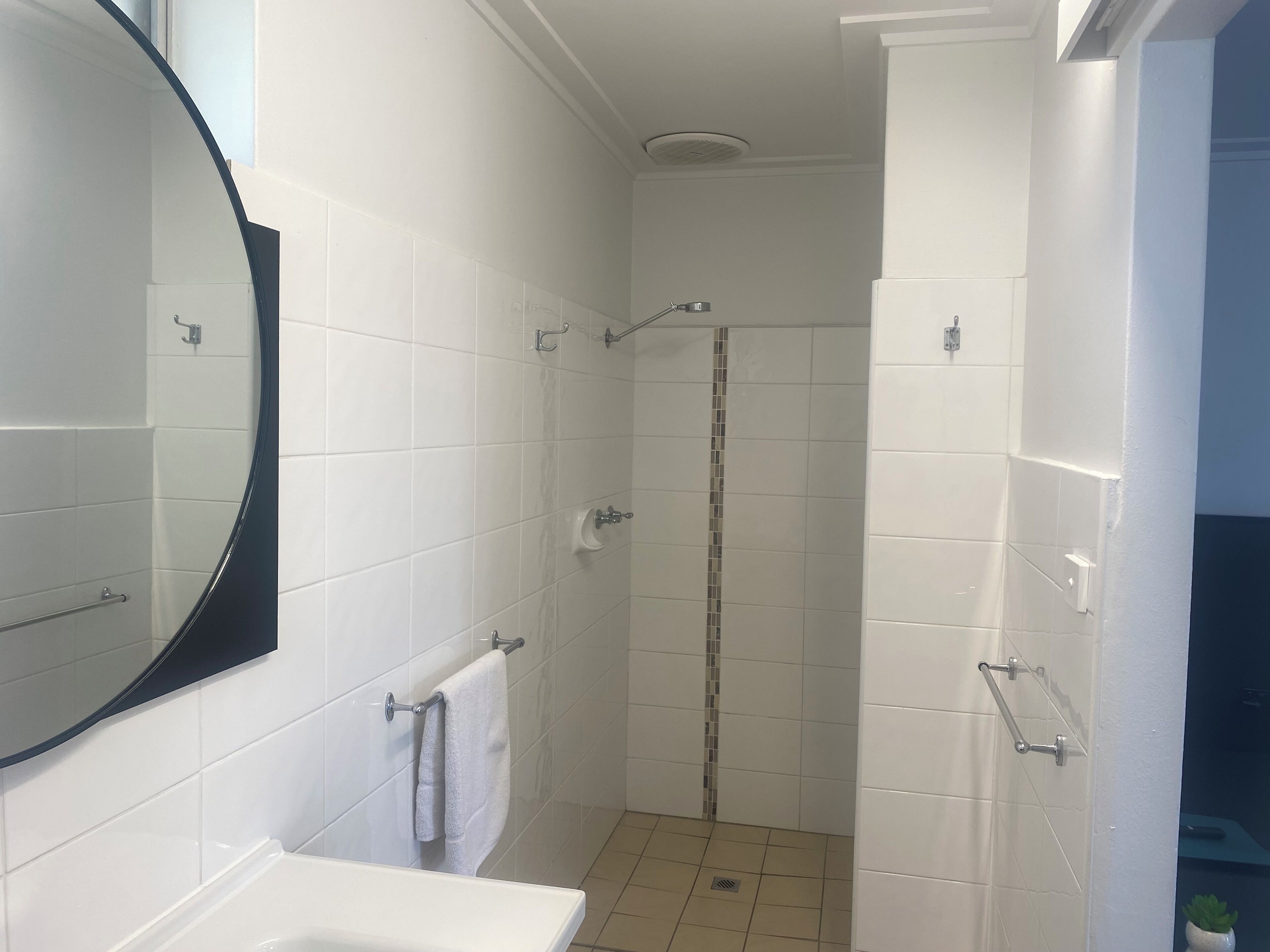 Un baño con azulejos blancos, un lavamanos blanco, un espejo, una ducha y un perchero para toallas.