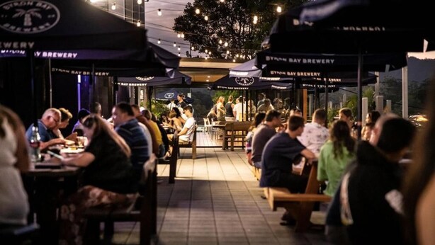 Un espace extérieur aménagé pour les repas, avec plusieurs tables et des parasols, entouré d’un mur de briques et d’un arbre.