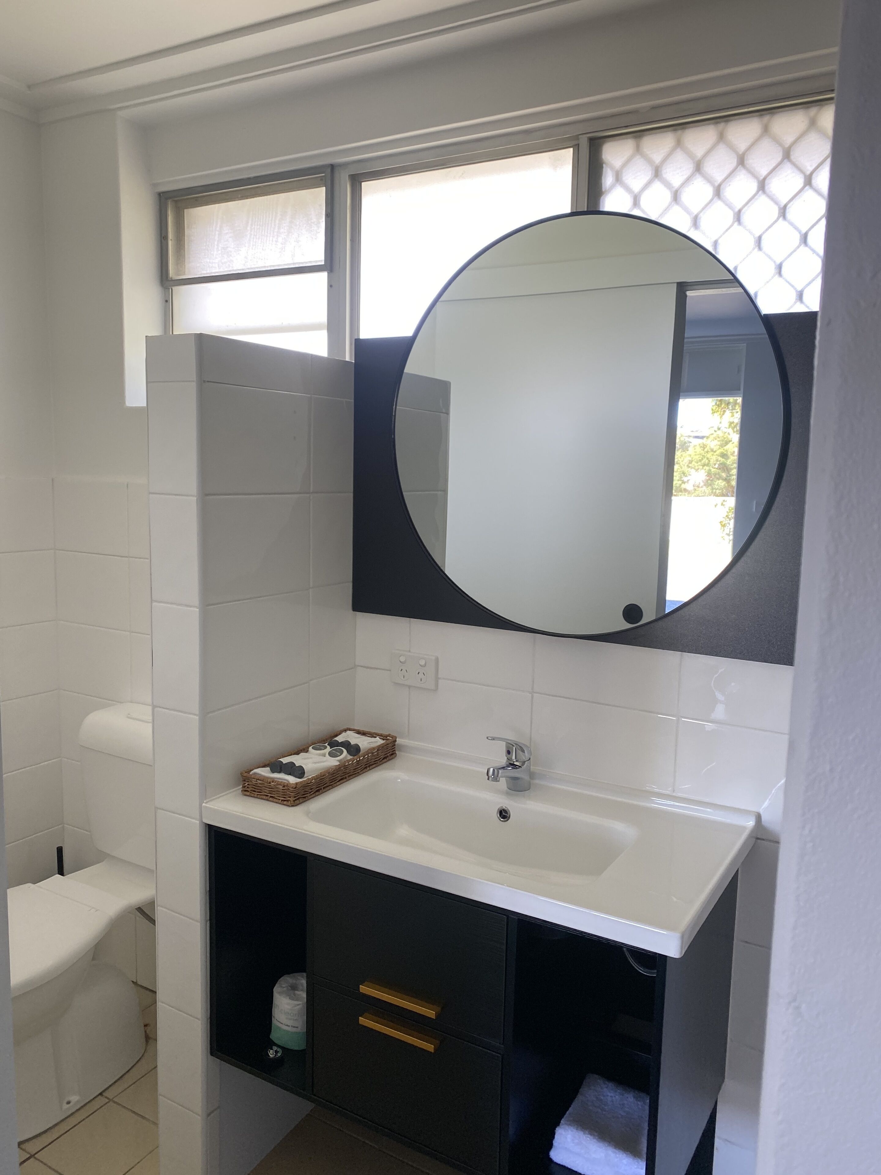 A bathroom with a white sink, a round mirror, and a toilet.