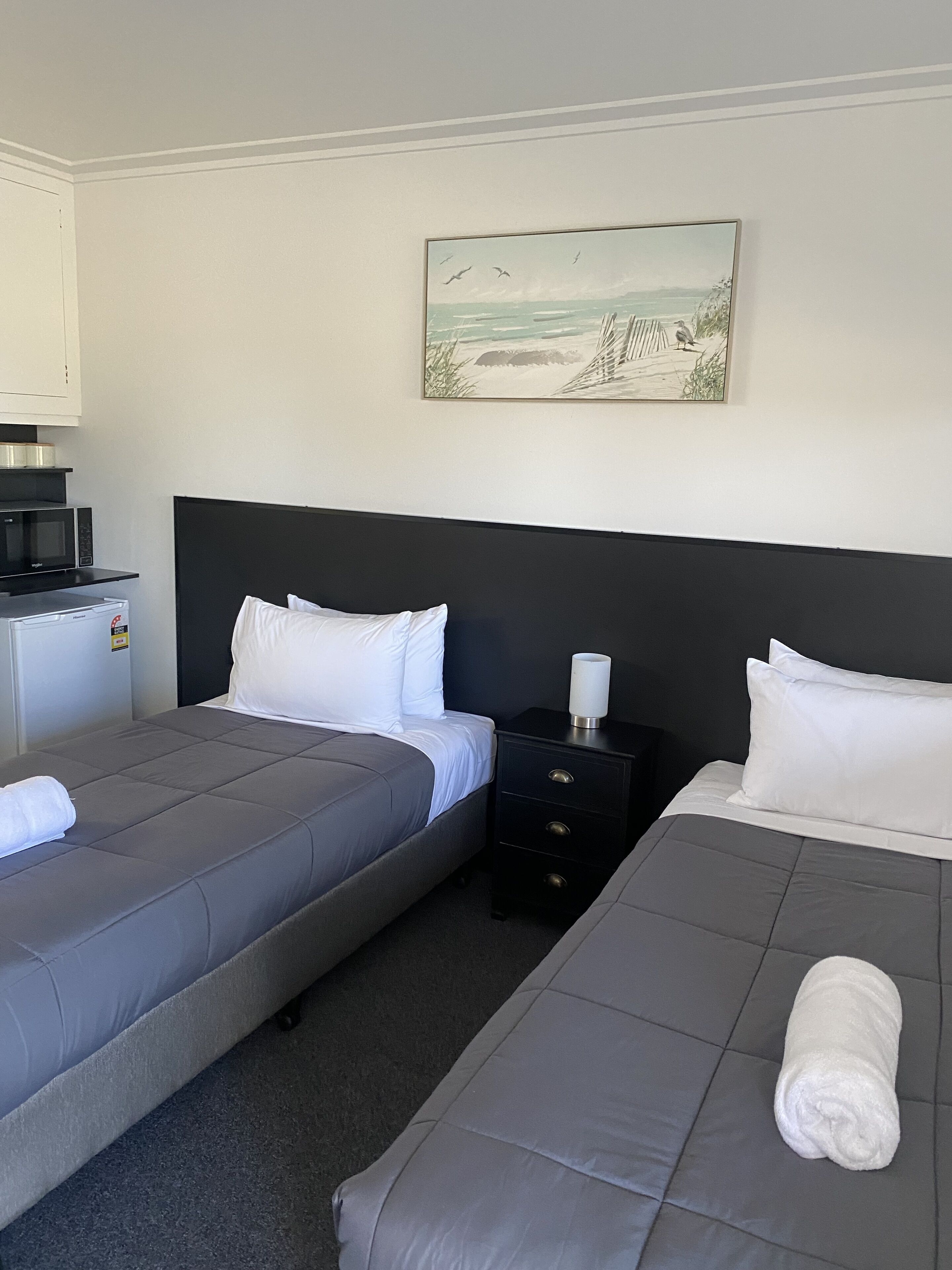 Et hotelværelse med to senge, et lille tekøkken og et maleri af en strand.
