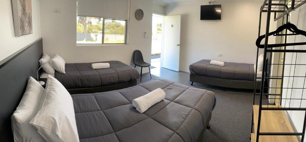A room with three beds, a chair, and a TV mounted on the wall.
