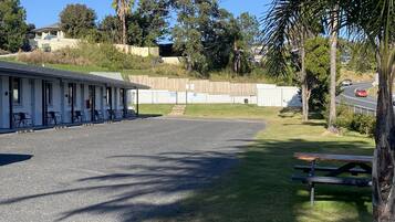 Un motel con una zona de estar al aire libre techada, un estacionamiento cercado y una carretera con vehículos.