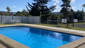 Une piscine rectangulaire dont les bords sont recouverts de petits galets, entourée d’une clôture et d’arbres.