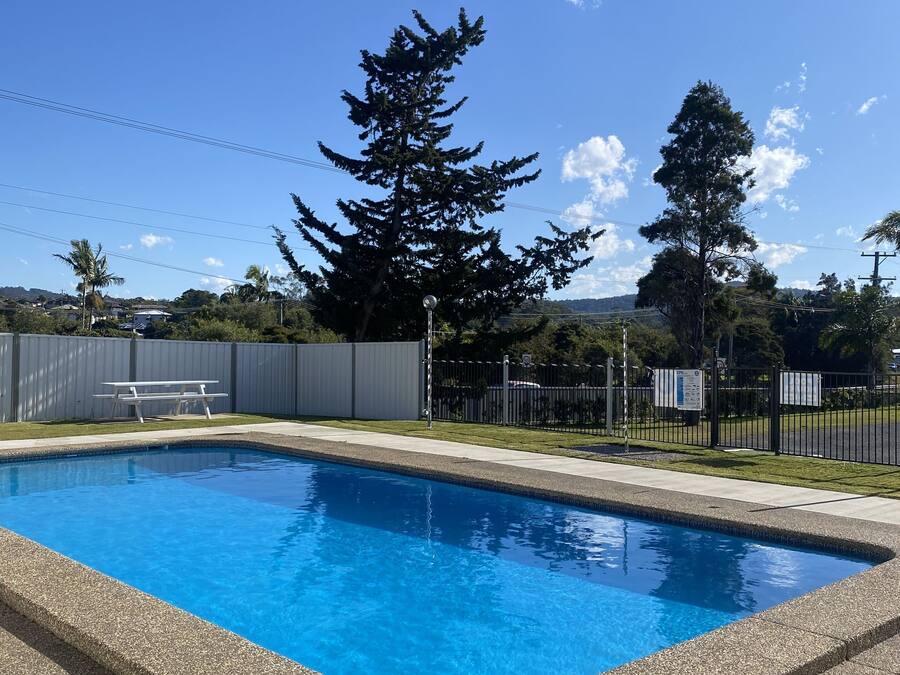 A rectangular swimming pool with a pebble-lined edge, surrounded by a fence and trees.