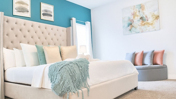 A bedroom with a tufted headboard, a bed with multiple pillows, a grey sofa, and a blue abstract painting on the wall. - Stylish Kissimmee Getaway Game Room – 99 Dollar Deal! (Kissimmee)