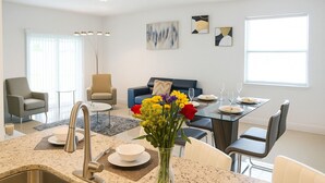 A modern living room with a dining area, featuring a kitchen with a sink and a vase of flowers. - Stylish Kissimmee Getaway Game Room – 99 Dollar Deal! (Kissimmee)