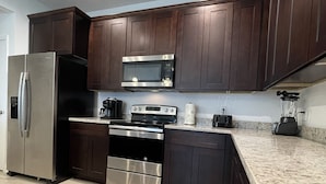 A modern kitchen with dark wooden cabinets, stainless steel appliances, and a granite countertop. - Stylish Kissimmee Getaway Game Room – 99 Dollar Deal! (Kissimmee)