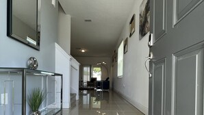 A hallway with a glass console table, a potted plant, and a grey door. - Stylish Kissimmee Getaway Game Room – 99 Dollar Deal! (Kissimmee)