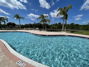 A clear blue swimming pool with a 4 FT depth marker, surrounded by palm trees and a fenced area with lounge chairs.