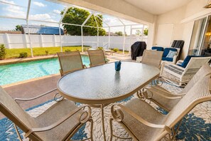 A covered outdoor area with a pool, a round glass table, and wicker chairs. - Gulfstream Villa | Heated Pool + Dog Friendly (Englewood)