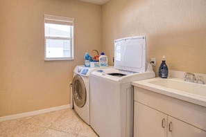 A laundry room with a front-loading washer and dryer, a sink, and laundry supplies. - Gulfstream Villa | Heated Pool + Dog Friendly (Englewood)