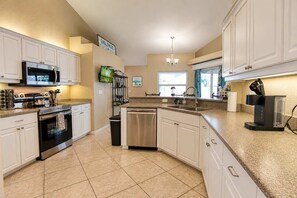 A modern kitchen with white cabinetry, stainless steel appliances, and a granite countertop. - Gulfstream Villa | Heated Pool + Dog Friendly (Englewood)