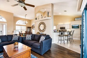 A spacious living room with a dark blue sofa, a wooden coffee table, and a ceiling fan. - Gulfstream Villa | Heated Pool + Dog Friendly (Englewood)