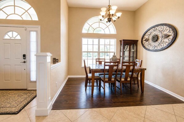A dining area with a wooden table and chairs, a chandelier, and a decorative wall piece. - Gulfstream Villa | Heated Pool + Dog Friendly (Englewood)