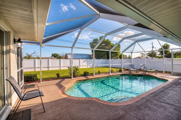 A covered outdoor swimming pool with a clear blue water feature, surrounded by a patio area with seating and a white fence in the background. - Gulfstream Villa | Heated Pool + Dog Friendly (Englewood)