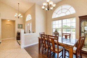 A dining area with a large table and chairs, a chandelier, and a view through large windows. - Gulfstream Villa | Heated Pool + Dog Friendly (Englewood)