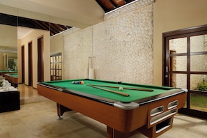 A pool table in a room with a stone wall and a large window. - Villa Nagasutra by Nakula (Kutuh)