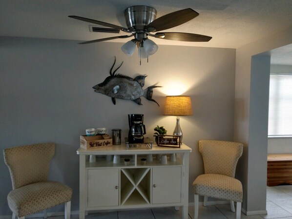 A room with two armchairs, a coffee station, a wall-mounted fish decoration, and a ceiling fan. - Sunrise, Suntan, Sunset repeat! Coastal getaway! 2 bd, pet friendly, fenced yard (Holiday)