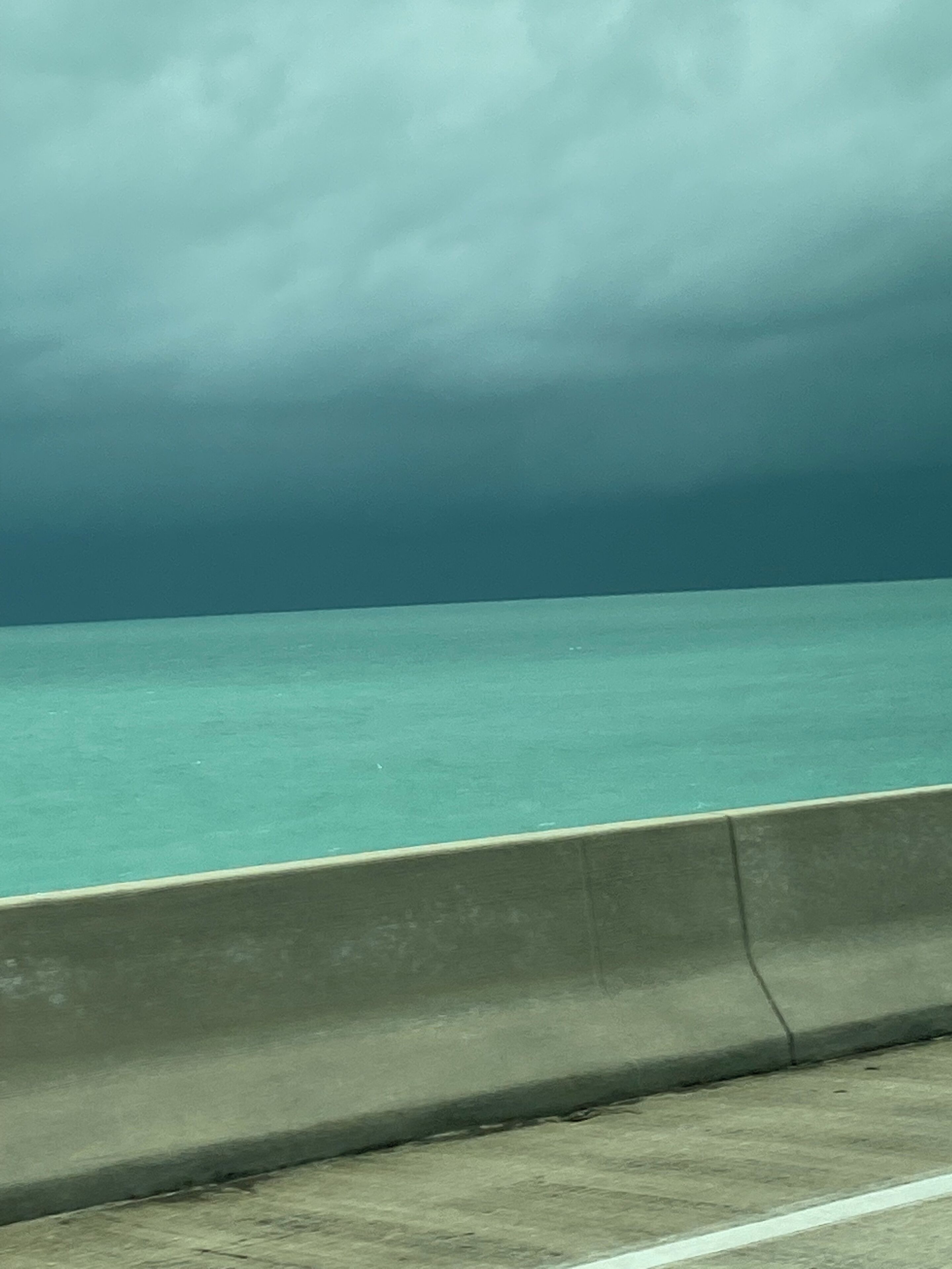 A concrete barrier with a view of a calm body of water under a cloudy sky.