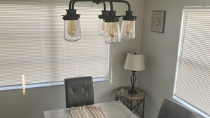 Comedor con mesa, sillas, lámpara colgante y ventana con persianas.