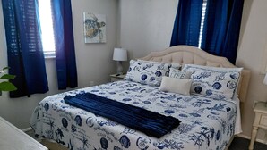 Un dormitorio con cama, cubierta con un edredón de motivos marinos en azul y blanco, una manta azul y almohadas a juego.