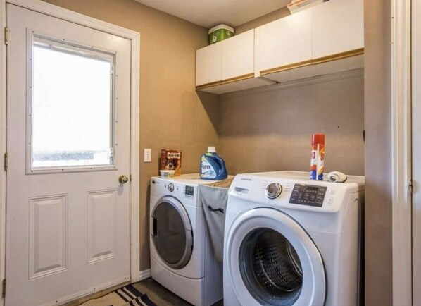 A laundry room with two front-loading washing machines, a window, and a cabinet above the machines.