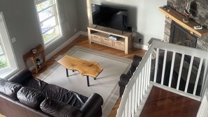 A spacious living room with a large flat-screen TV, a stone fireplace, a wooden coffee table, and a leather sofa. - Fantastic Lake Views and Gorgeous Sunsets All year round (Nestleton Station)