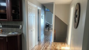 A spacious kitchen with dark wooden cabinets and a tiled backsplash, leading to a hallway with wooden flooring and a large wall clock. - Fantastic Lake Views and Gorgeous Sunsets All year round (Nestleton Station)