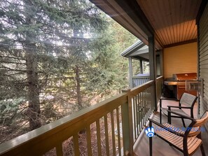 A wooden deck with a bench and a grill, overlooking a forested area.