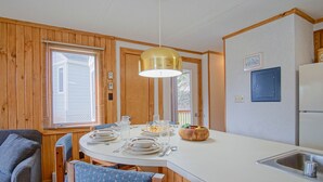 Una cucina compatta con rivestimenti in legno, un piano di lavoro bianco, un lavello e un'area pranzo con sedie e tavolo apparecchiato per due.