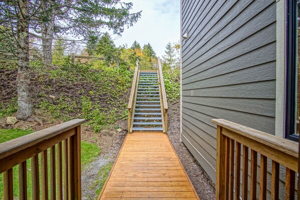 A wooden deck leading to a staircase with a view of a house and surrounding trees.
