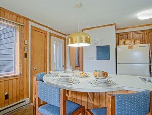 Une cuisine compacte avec un lambris en bois, une table blanche dressée pour le repas et un réfrigérateur encastré.