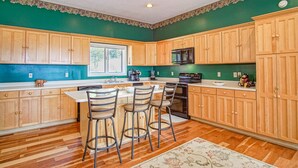 Una cocina con armarios de madera, una isla central con taburetes de bar, un microondas y un lavavajillas.