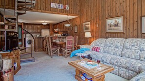 Un interior acogedor de cabaña con una escalera de madera, un comedor, un sofá y una mesa de centro.