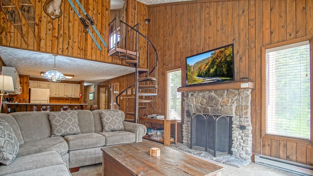 Una sala de estar acogedora con chimenea de piedra, un televisor de pantalla plana grande, una escalera de madera y un sofá seccional.