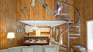 Un interior de madera con una escalera de caracol, un comedor y un sofá con cojines estampados.
